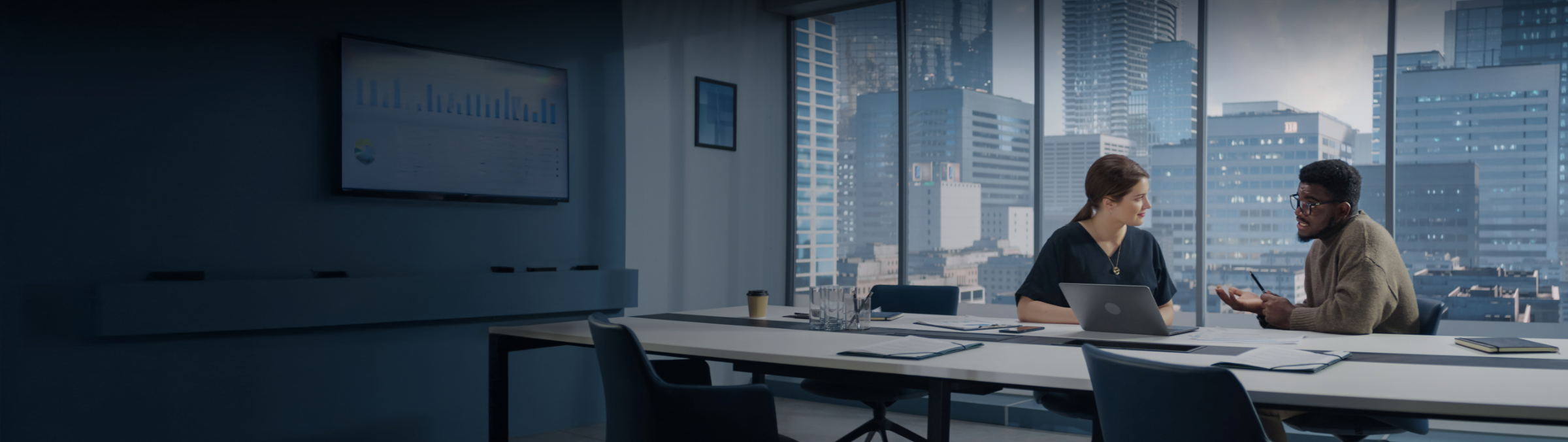 Two business professionals discussing energy market strategy in a city-view conference room