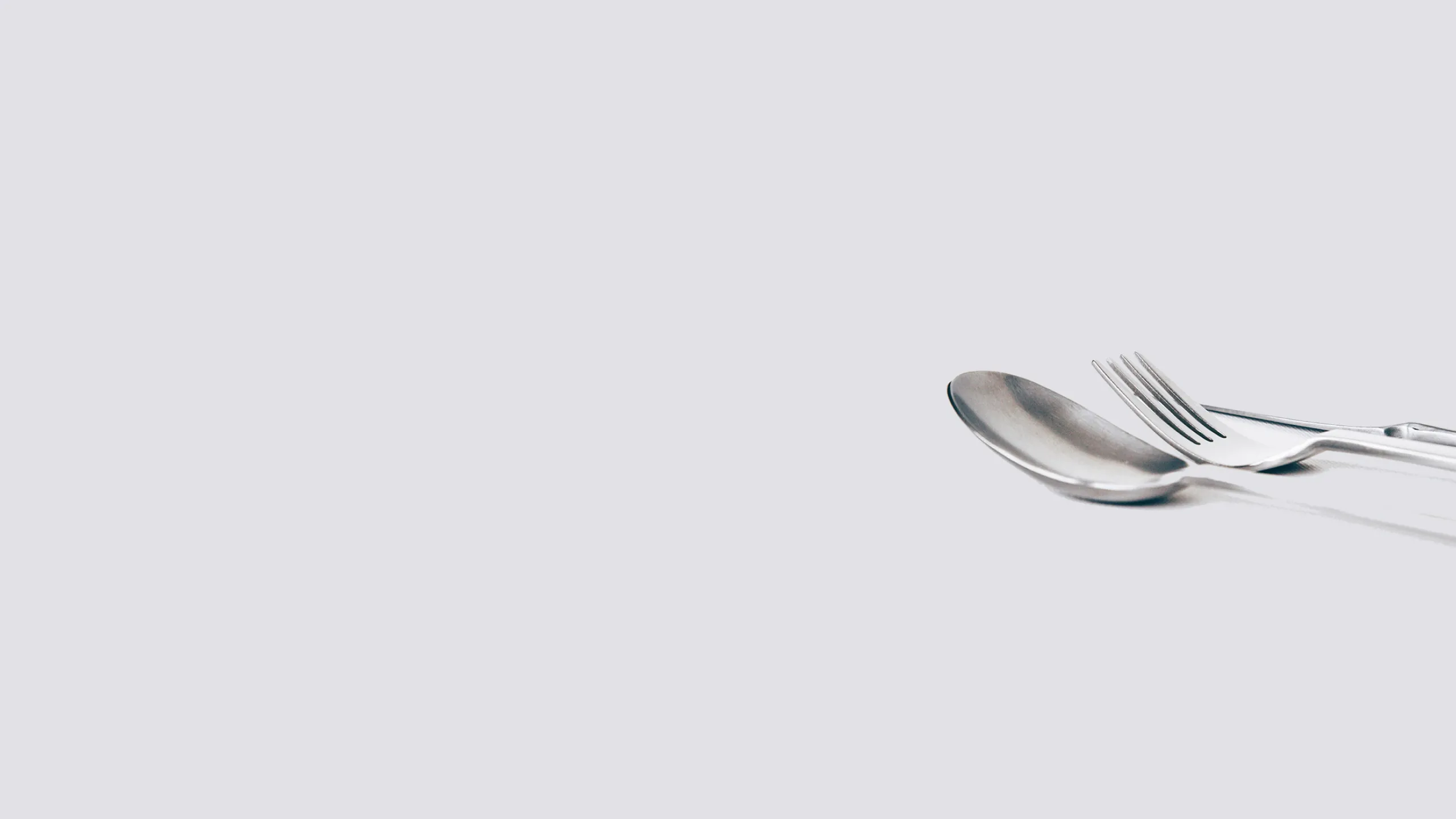 close up of metal spoon, fork, and knife on white surface