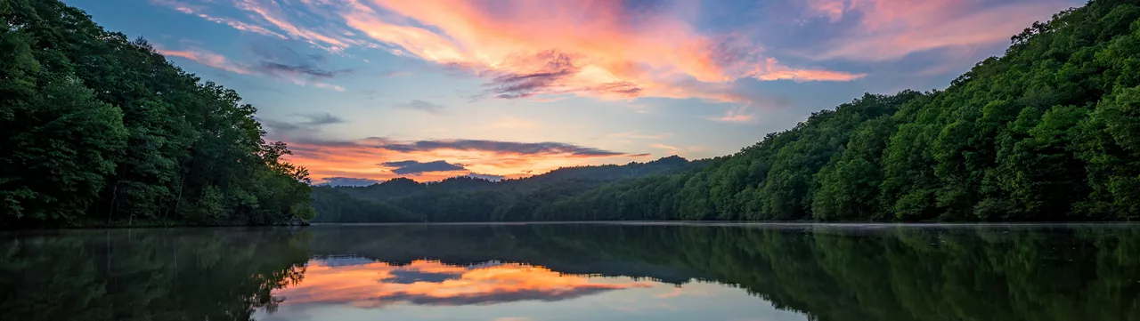 Forest-covered-hills-surrounding-a-lake-at-sunset