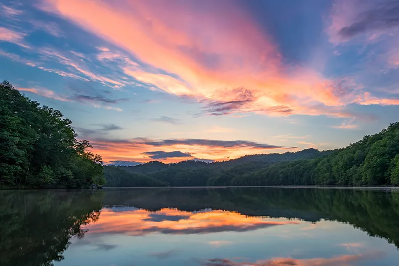 Forest-covered-hills-surrounding-a-lake-at-sunset