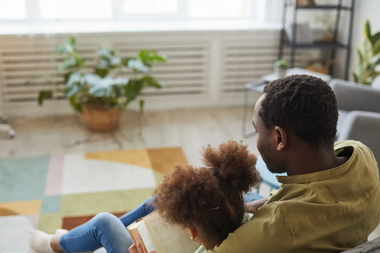father and daughter reading together on couch.