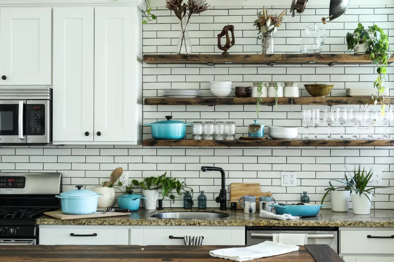 Bright modern kitchen with white cabinets, open wooden shelves, plants, and cookware