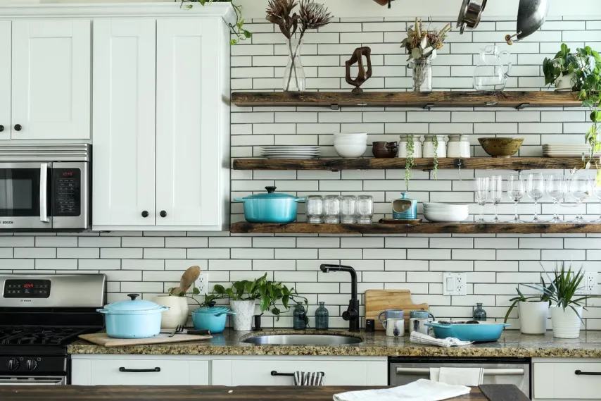 Bright modern kitchen with white cabinets, open wooden shelves, plants, and cookware