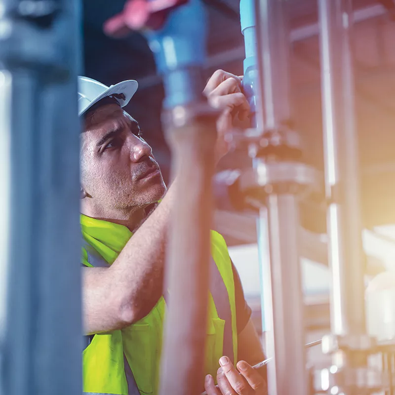 worker in a hard hat and safety vest adjusts pipes in an industrial setting.