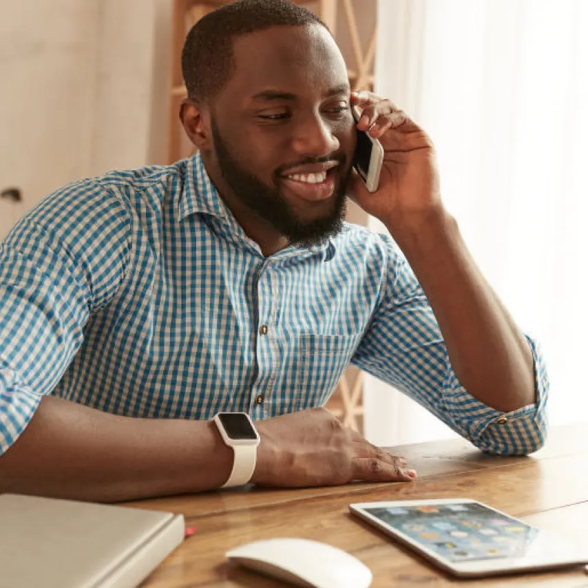 man speaking on mobile phone while sitting at table with tablet and mouse.