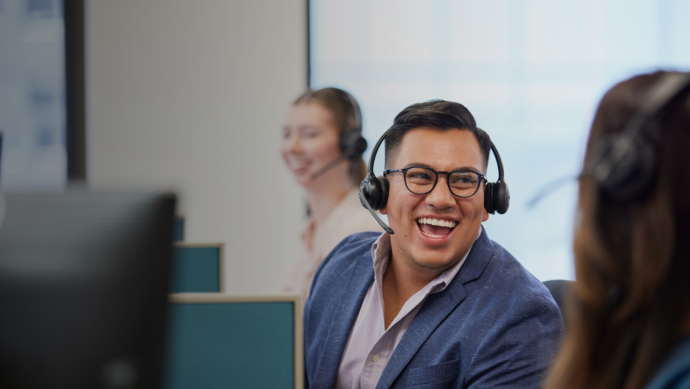 male-employee-with-headset-lauging-along-with-coworkers-at-desk