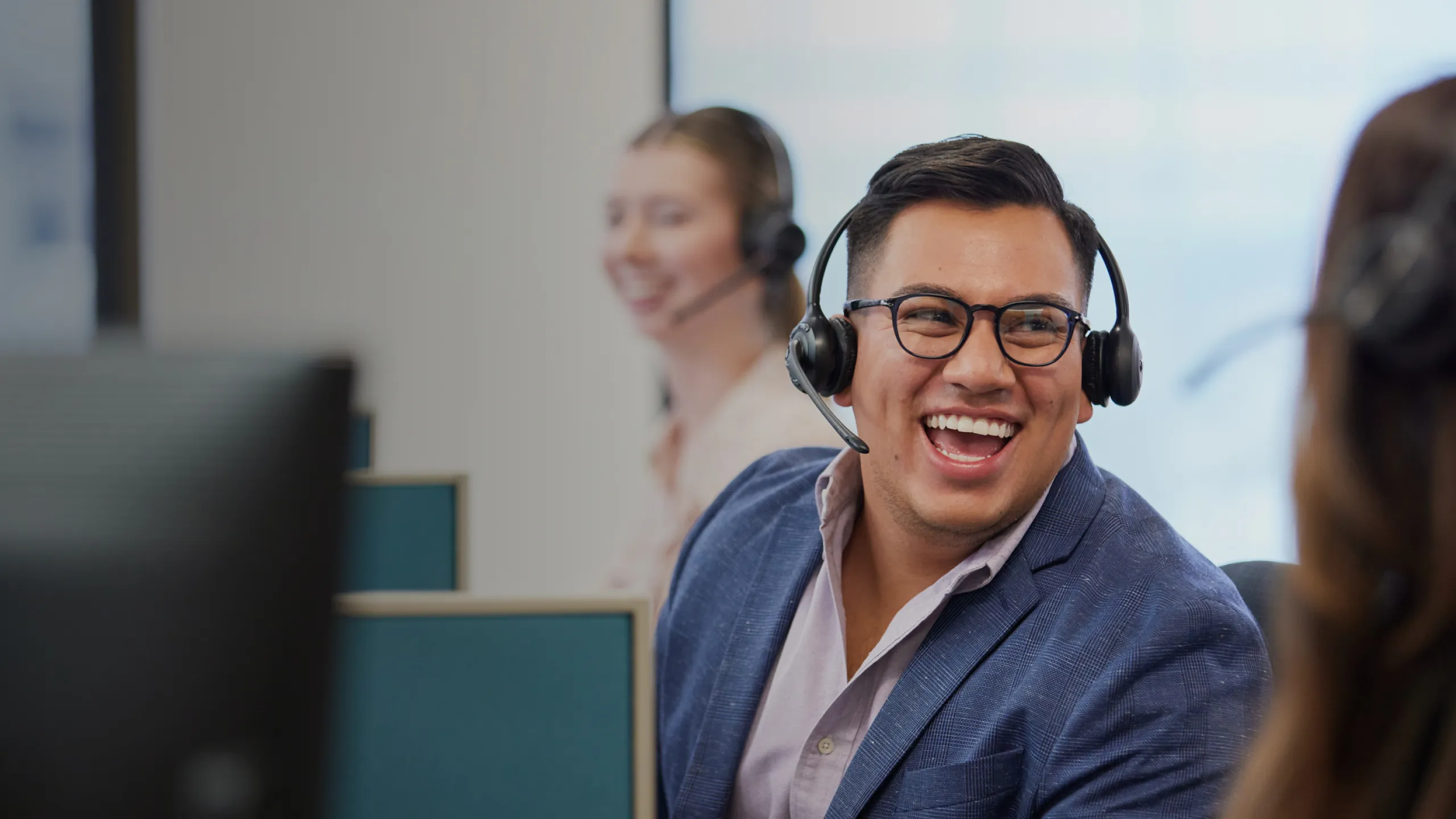 male-employee-with-headset-lauging-along-with-coworkers-at-desk