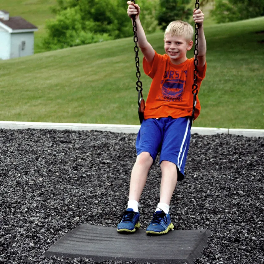 child smiling on swing in rubber filled playground.