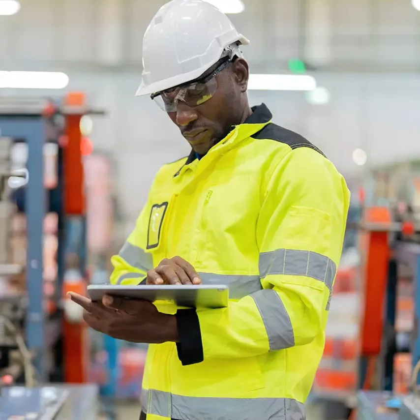 male factory worker in hard hat looking at tablet