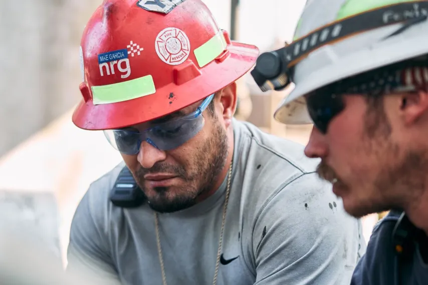 two plant workers wearing hard hats performing maintenance detail.