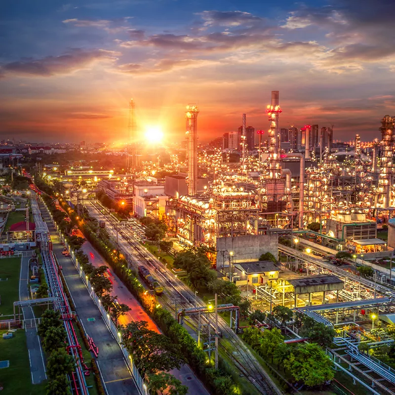 sunset over an industrial refinery complex with bright lights and metal structures, viewed from above.