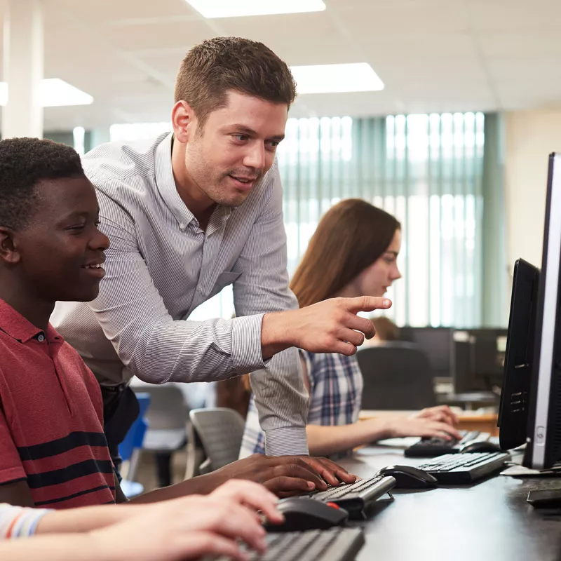 educator-talking-to-students-while-pointing-at-computer-screen