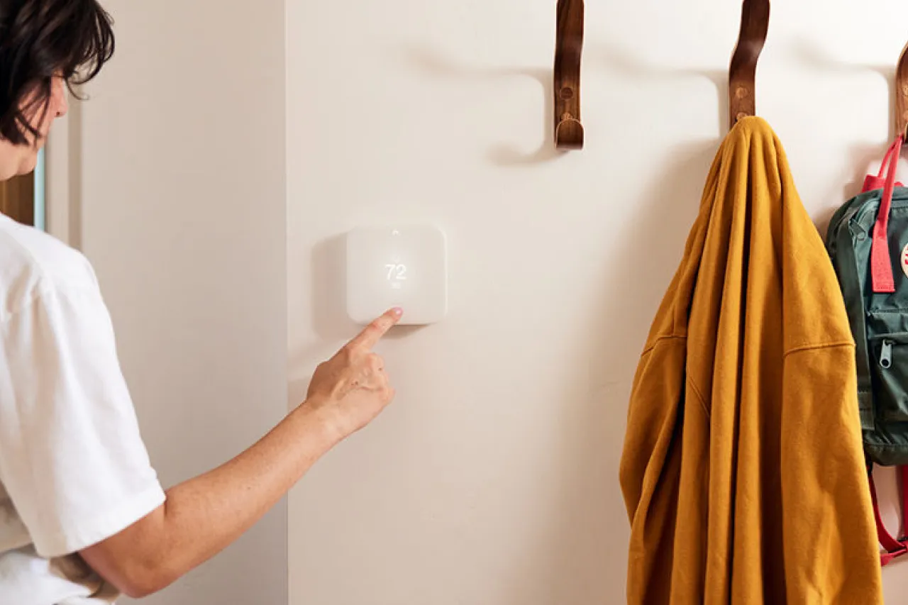 woman adjusting Vivint thermostat next to coat hangers.