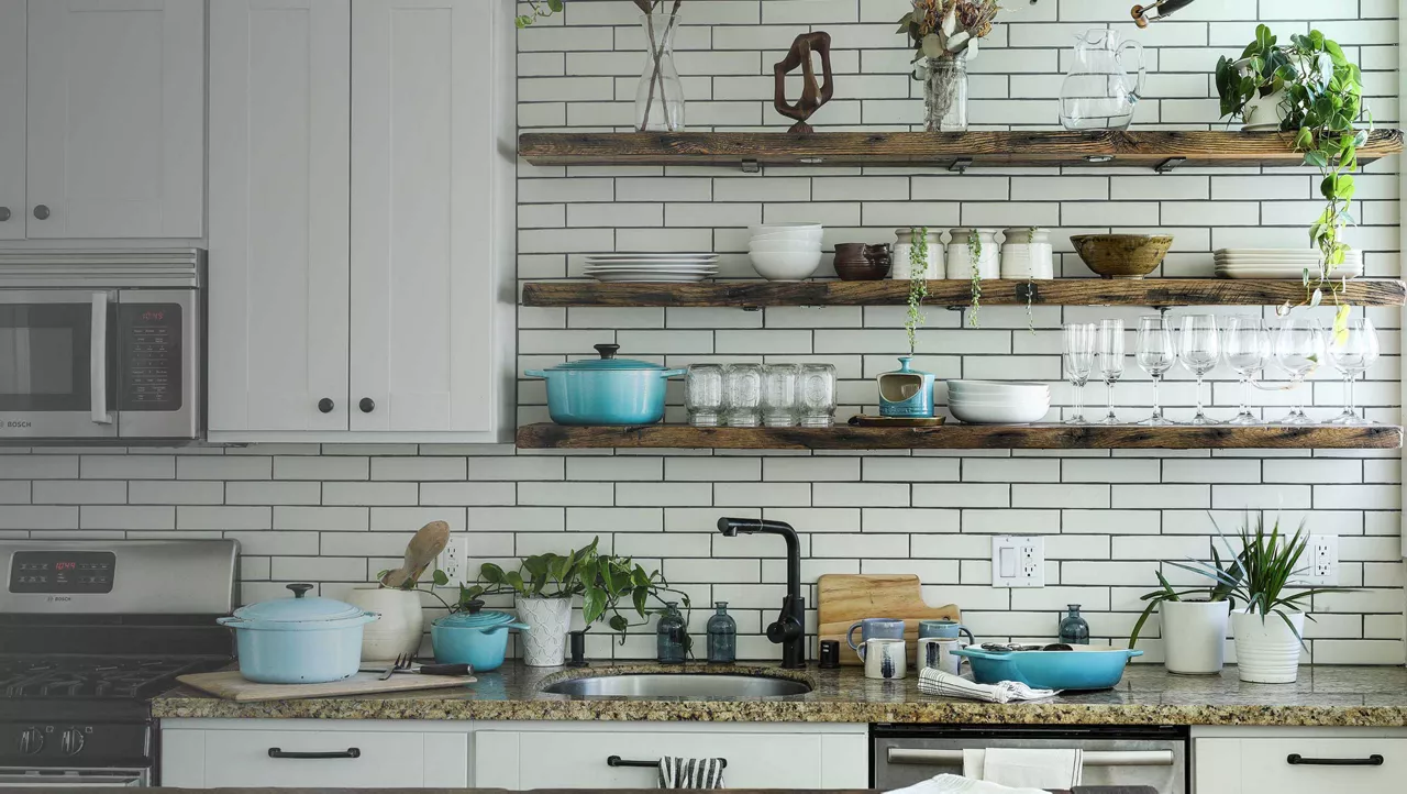 Bright modern kitchen with white cabinets, open wooden shelves, plants, and cookware