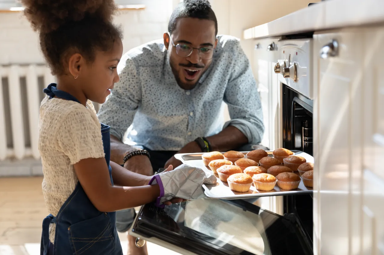 father and daughter baking together pulling muffins out of oven.