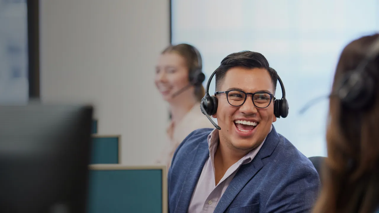 male employee with headset lauging along with coworkers at desk.
