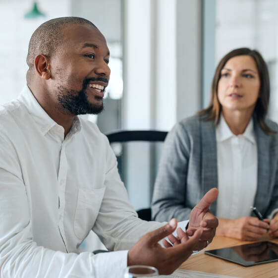 man speaking and gesturing while woman listens in an office meeting setting.