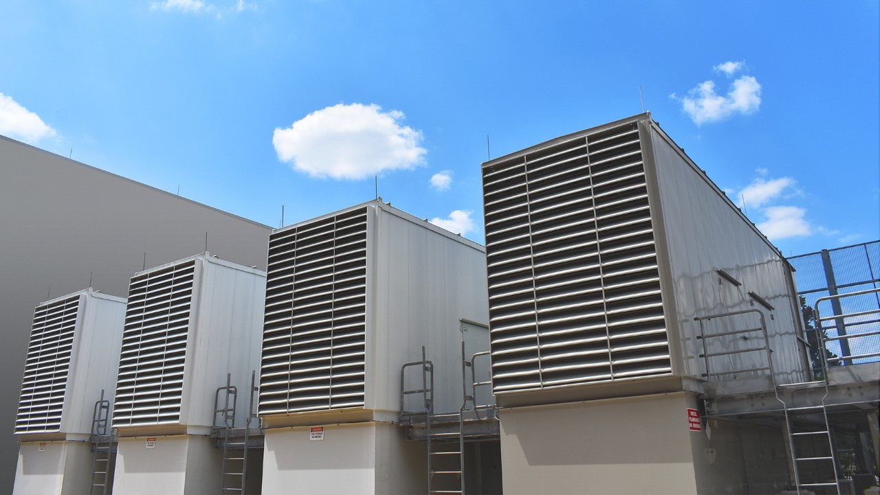 four large industrial HVAC units outside a building under a blue sky with scattered clouds.