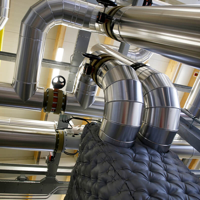 shiny metal ventilation pipes and insulated ducts inside an industrial building, seen from below.