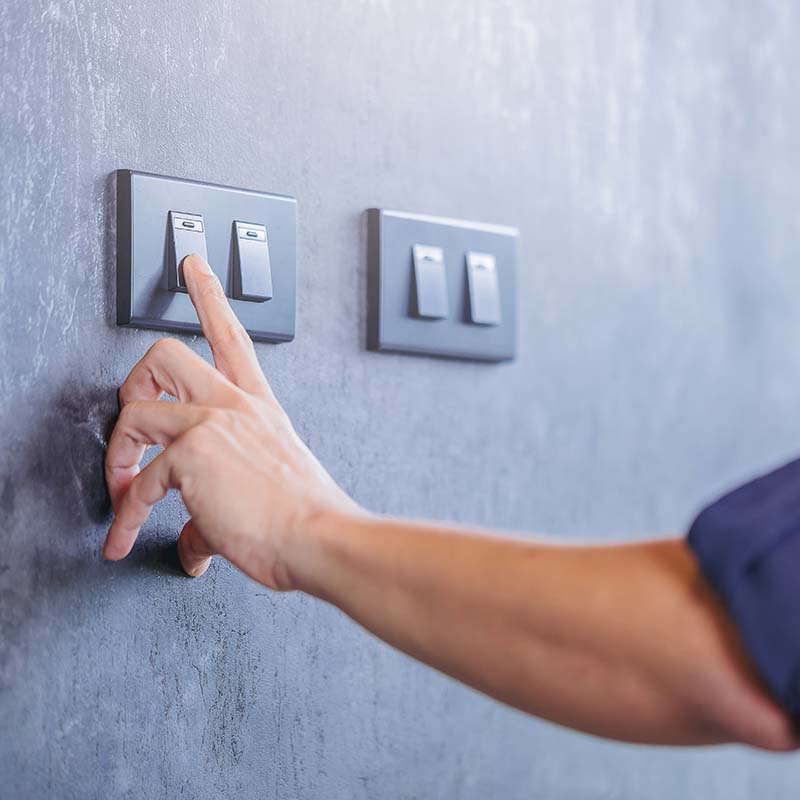 a persons hand is flipping a light switch on a gray wall, next to another set of switches.