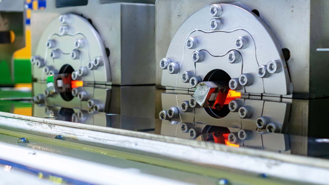 close-up of industrial machine with metal parts and orange glowing section, possibly during manufacturing process.