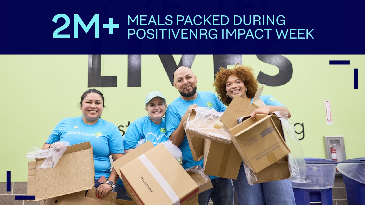 four smiling people in blue shirts hold empty boxes under a sign about meals packed during PositIvenrg Impact Week.