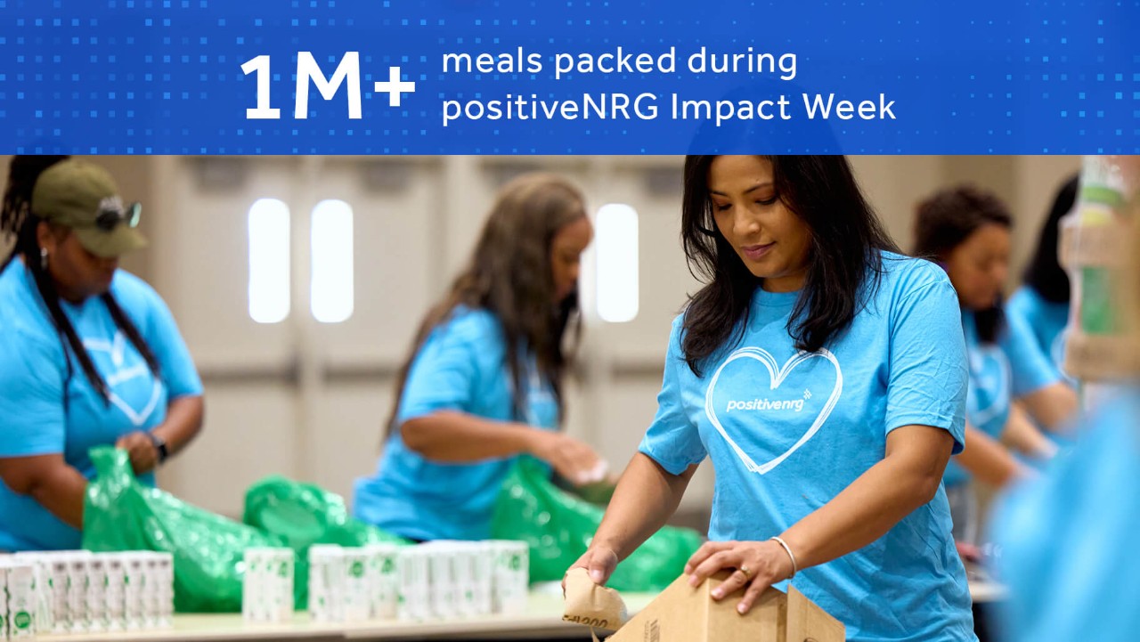 volunteers in blue shirts pack food during positiveNRG Impact Week, with a sign noting 1M+ meals packed.