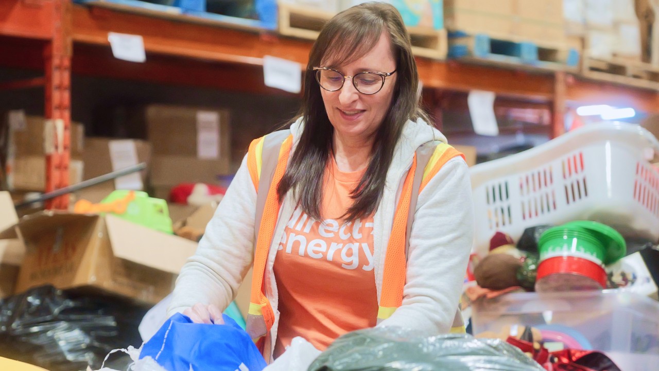 woman wearing glasses and a vest sorts donated items in a warehouse full of boxes, clothes, and baskets.
