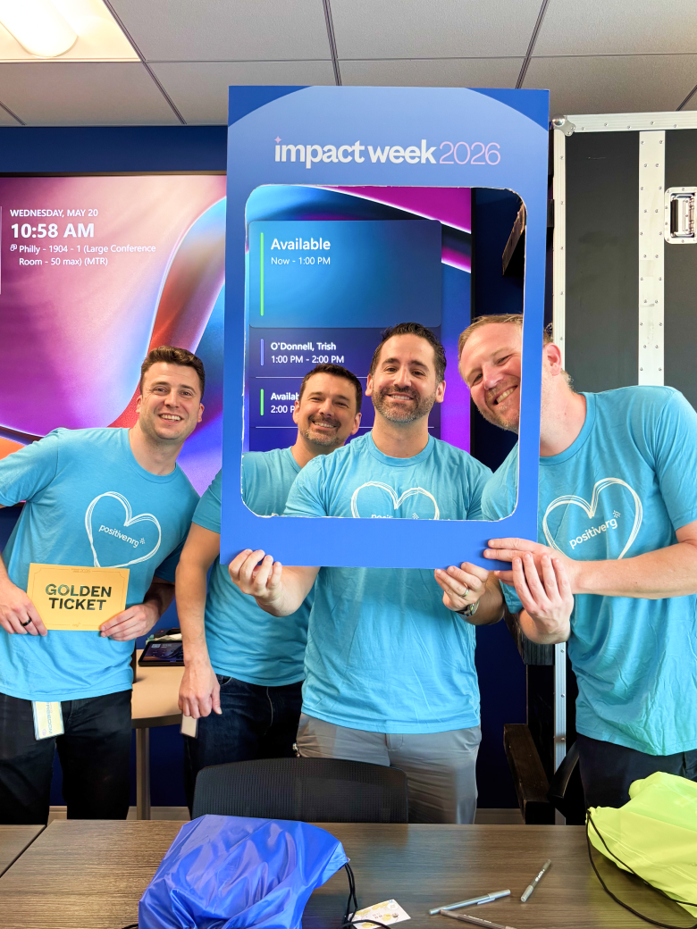 four smiling men in matching blue shirts pose with a large Impact Week 2026 frame at an event.