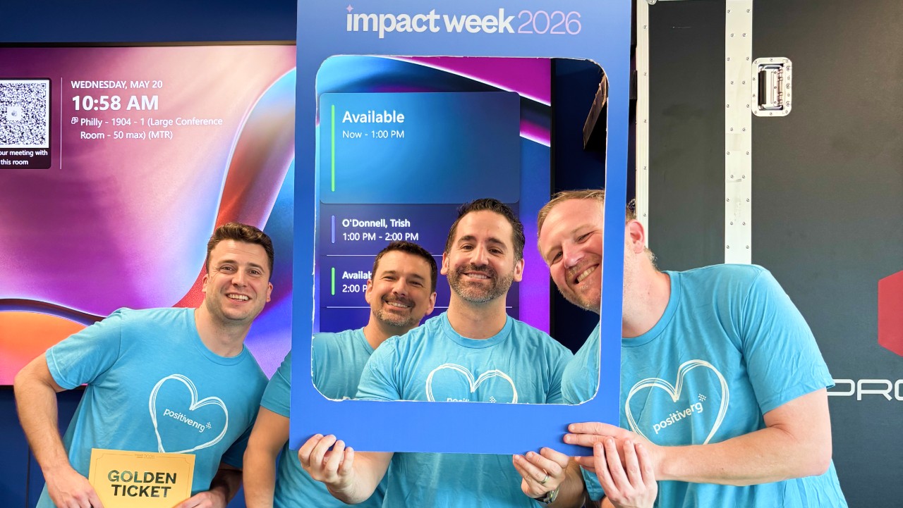 four smiling men in matching blue shirts pose with a photo frame at an event called Impact Week 2026.
