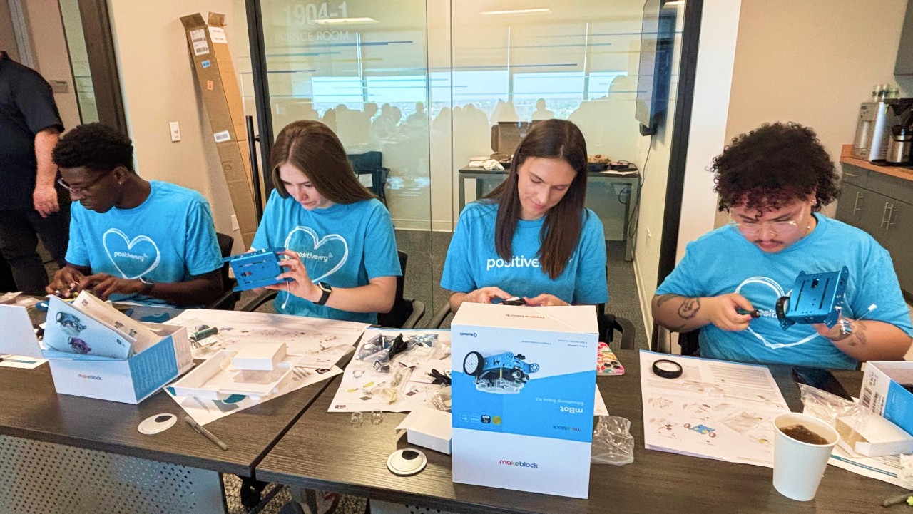 four people in blue shirts assembling robotics kits at a table with instructions and parts.