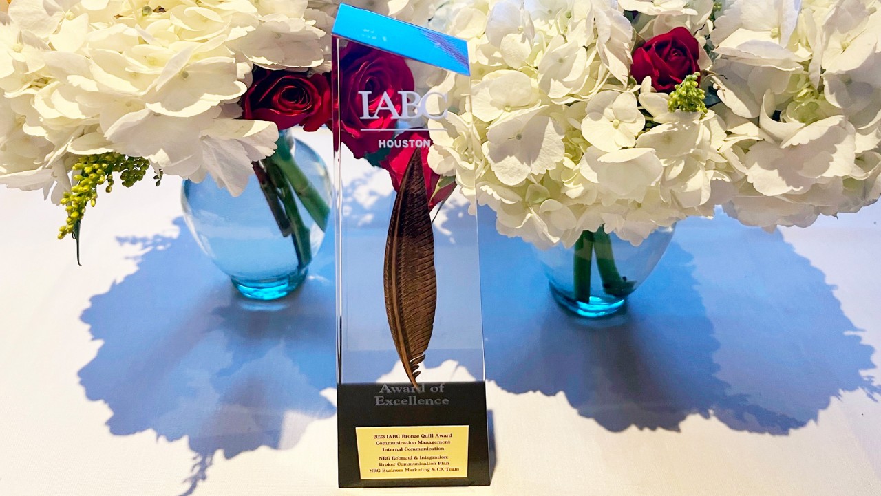 a glass IABC Houston Award of Excellence trophy on a table, flanked by white and red flower arrangements.