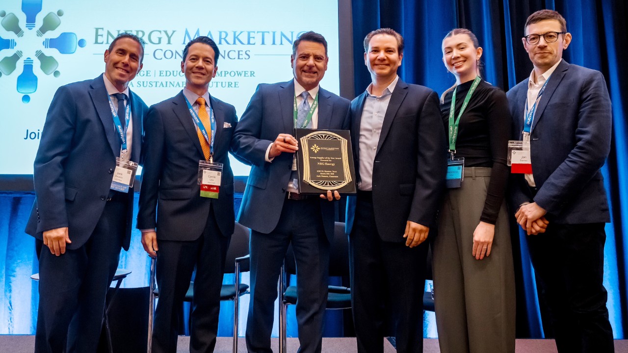 six people stand onstage, smiling, with one holding a plaque at an energy marketing conference.