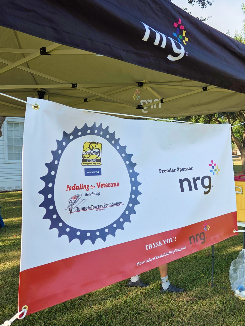 banner for Pedaling for Veterans event, sponsored by NRG, displayed under a canopy outdoors.