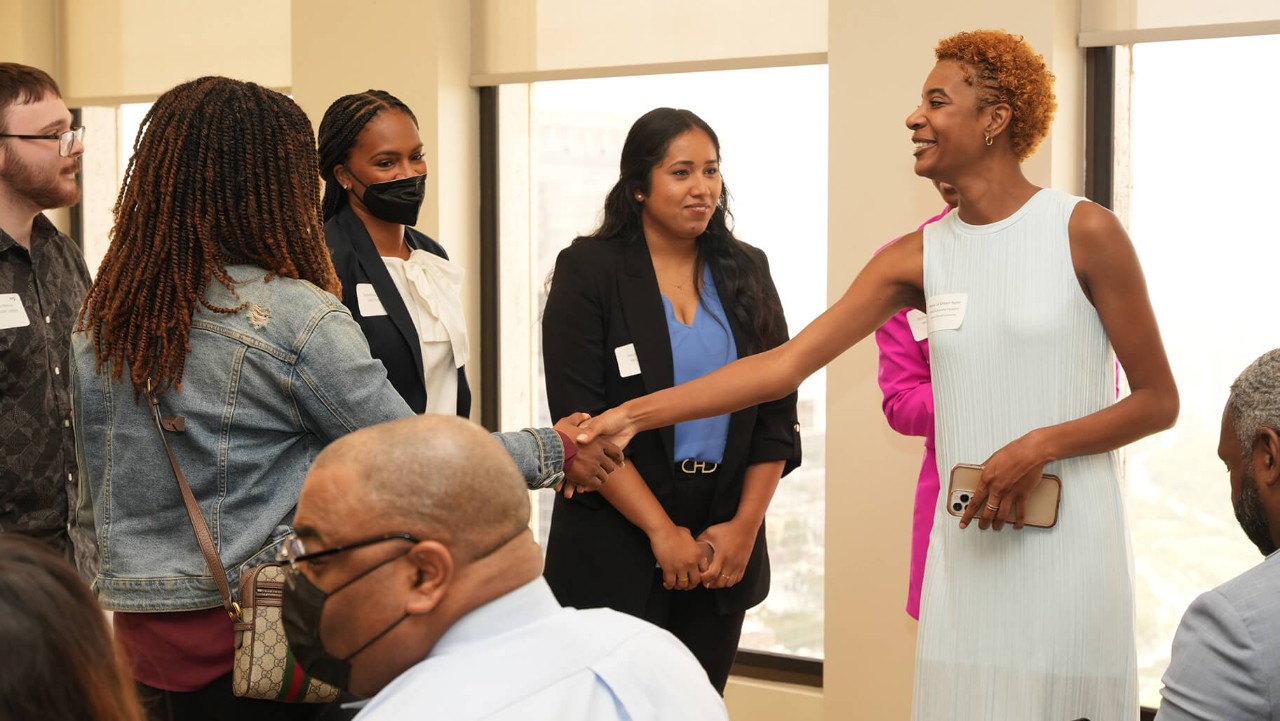a woman in a white dress shakes hands with another woman in a group at an indoor event.