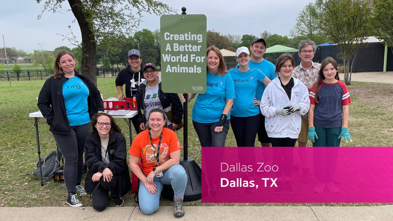 group smiling outdoors by a sign reading Creating A Better World For Animals at Dallas Zoo.
