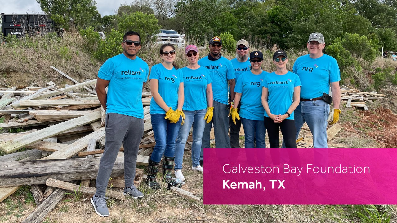 eight people in blue shirts and yellow gloves pose outdoors by a pile of wooden debris; text: Kemah, TX.