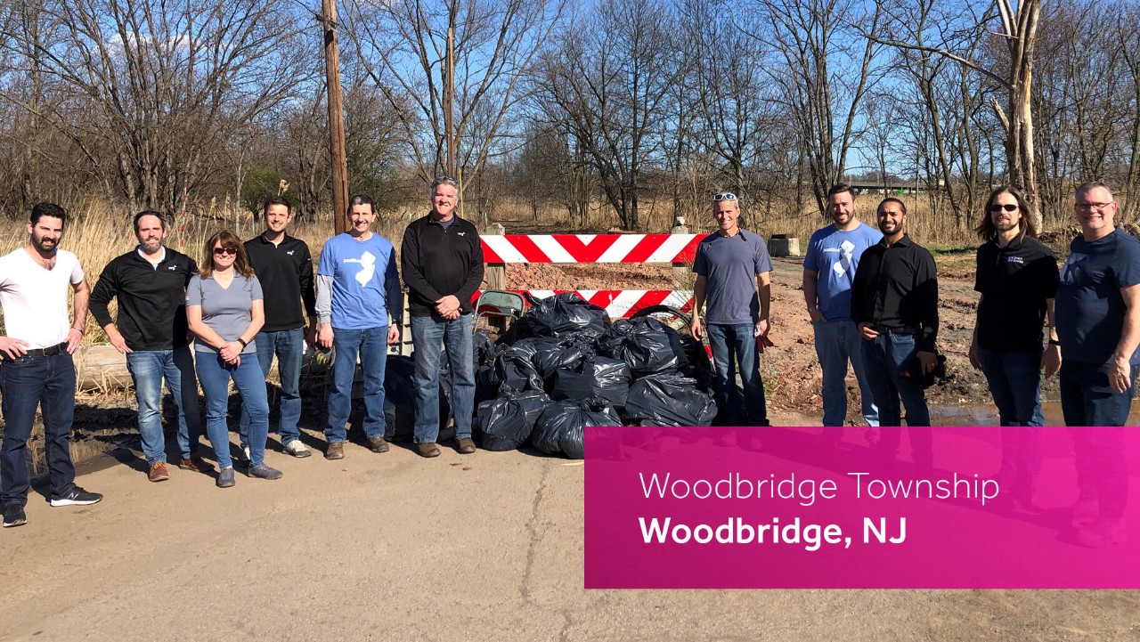 a group of people stands near garbage bags after a cleanup in Woodbridge Township, NJ, on a sunny day.