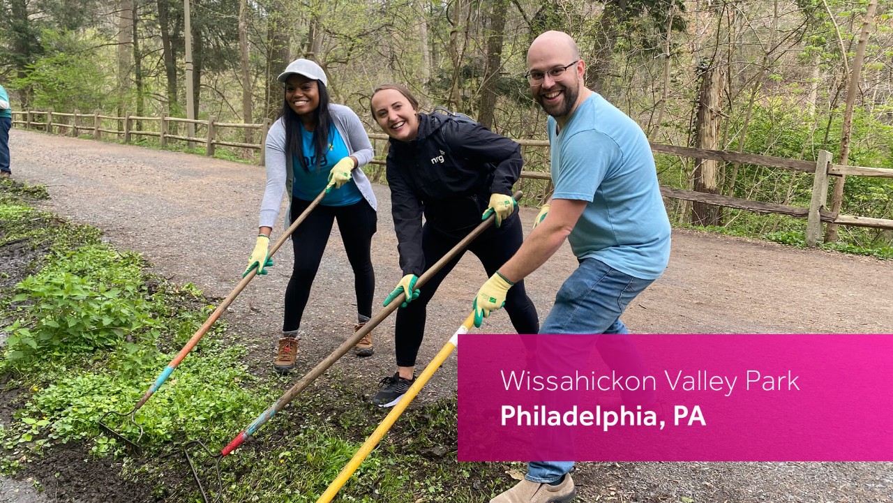 three people with rakes smile while volunteering outdoors at Wissahickon Valley Park in Philadelphia, PA.