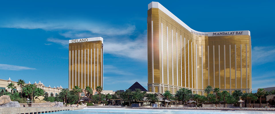 gold-colored Delano and Mandalay Bay hotel towers with palm trees and a pool under a clear blue sky.