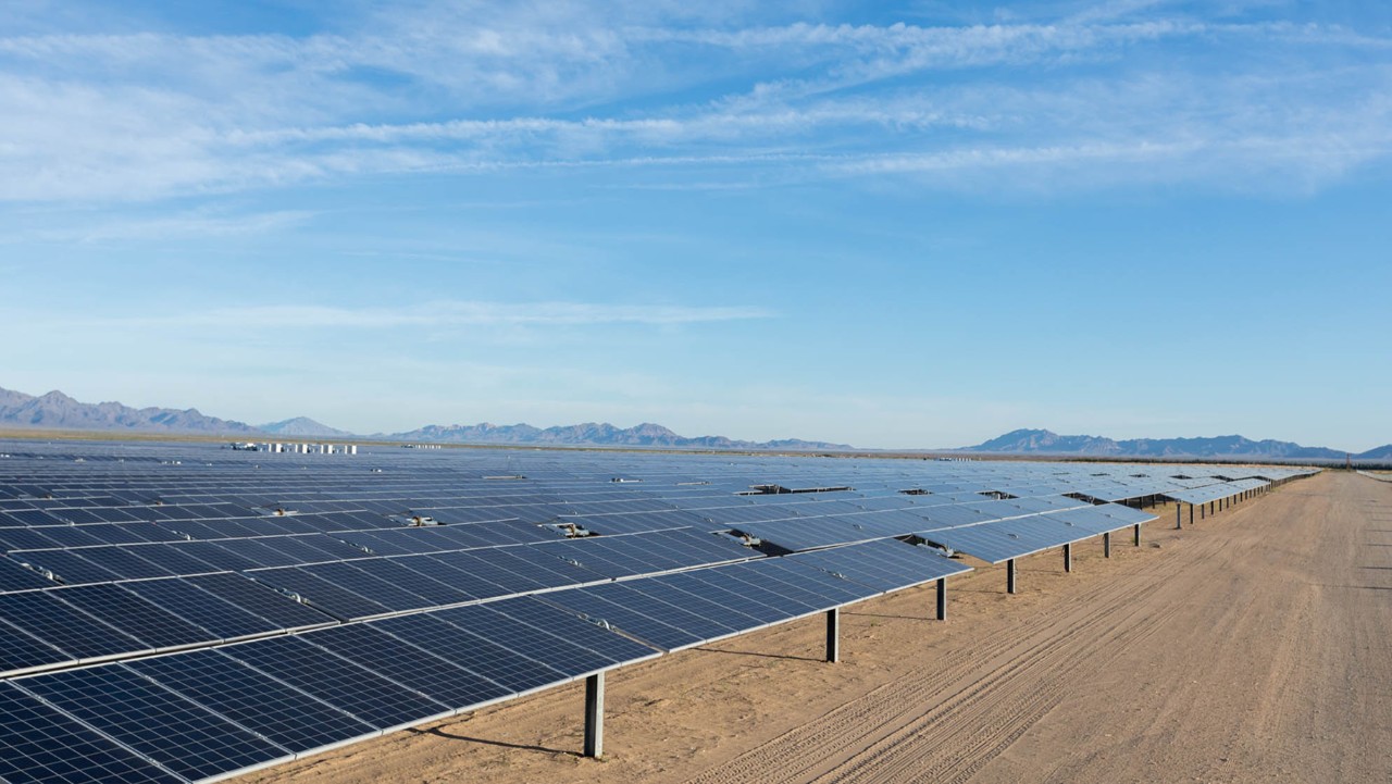 rows of solar panels on a vast desert landscape under a clear blue sky.